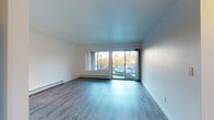 Located at 10800 SW Canterbury Ln in Tigard, Oregon, this single-floor residence offers a clean, modern interior with a thoughtfully designed open layout. Throughout the home, light-toned laminate wood flooring provides a cohesive and contemporary aesthetic.

The spacious living area is a standout feature, filled with natural light from a large picture window and sliding glass door that opens to views of the surrounding neighborhood. A baseboard heating system runs along the exterior wall, ensuring year-round comfort.

The kitchen is well-appointed with white shaker-style cabinetry, dark countertops, a stainless steel range, dishwasher, and a built-in range hood — all complemented by a bold teal accent backsplash that adds a pop of color to the space.

A hallway connects the living and kitchen areas to the bedroom and bathroom. The bedroom is a comfortable, well-lit room featuring a ceiling fan with light fixture, a window with exterior views, and a large sliding-door closet with a full-width hanging rod and shelf for ample storage.

The bathroom is clean and functional, featuring a full-size soaking tub with shower combo, brushed nickel fixtures and grab bar, a toilet, and wood-look tile flooring. An in-unit laundry area is also visible in the floor plan, adding everyday convenience to this well-maintained Tigard residence.