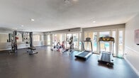 Located at 8561 De Soto Ave in Los Angeles, CA, this single-floor fitness center is a well-equipped facility designed to support a comprehensive workout experience. The space is finished with durable dark rubber flooring throughout, providing a practical and professional gym environment suited for a variety of exercise activities.

The main workout area is generously proportioned and features a diverse selection of fitness equipment, including treadmills, elliptical trainers, stationary and cycling bikes, a multi-station cable strength machine, and adjustable weight benches. A wall-mounted mirror on one side enhances the sense of space and supports proper form during strength training sessions.

Natural light floods the interior through a series of large glass doors and windows that line one wall, offering direct views of an outdoor swimming pool and surrounding landscaped areas. These doors also provide convenient access to the pool deck, creating a seamless connection between indoor and outdoor amenities.

The walls are finished in neutral gray tones with clean white trim, contributing to a calm and focused atmosphere. Recessed lighting supplements the natural light, ensuring the space remains well-illuminated at all times. An additional open area toward the rear of the facility offers flexible space for stretching, floor exercises, or future equipment. Security is supported by ceiling-mounted surveillance cameras throughout.