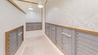Located at 2509 N. Davidson St. in Charlotte's NoDa neighborhood, this dedicated mail room offers a thoughtfully designed, single-floor space built to serve a multi-unit property. The room is organized around a central island structure, which itself houses rows of individual mailboxes, while additional banks of gray metal mailboxes with warm wood trim line the surrounding walls on multiple sides. The layout provides efficient circulation paths between the island and wall-mounted units, allowing easy access from all angles.

The interior finishes strike a balance between functionality and aesthetics. Light-toned tile flooring complements the crisp white walls, while a subtly patterned, tone-on-tone wallpaper adds a refined decorative touch above the mailbox banks. Wood trim framing each mailbox cluster introduces warmth and a cohesive design element throughout the space.

Overhead, a mix of modern geometric pendant lights and classic dome-style pendants provide ample, well-distributed illumination. The combination of fixture styles adds visual interest to the ceiling plane while ensuring the room remains bright and easy to navigate. The overall ambiance is clean, organized, and welcoming — a functional amenity space that reflects careful attention to both practical design and interior aesthetics.