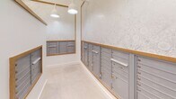 Located at 2509 N. Davidson St. in Charlotte's NoDa neighborhood, this dedicated mail room offers a thoughtfully designed, single-floor space built to serve a multi-unit property. The room is organized around a central island structure, which itself houses rows of individual mailboxes, while additional banks of gray metal mailboxes with warm wood trim line the surrounding walls on multiple sides. The layout provides efficient circulation paths between the island and wall-mounted units, allowing easy access from all angles.

The interior finishes strike a balance between functionality and aesthetics. Light-toned tile flooring complements the crisp white walls, while a subtly patterned, tone-on-tone wallpaper adds a refined decorative touch above the mailbox banks. Wood trim framing each mailbox cluster introduces warmth and a cohesive design element throughout the space.

Overhead, a mix of modern geometric pendant lights and classic dome-style pendants provide ample, well-distributed illumination. The combination of fixture styles adds visual interest to the ceiling plane while ensuring the room remains bright and easy to navigate. The overall ambiance is clean, organized, and welcoming — a functional amenity space that reflects careful attention to both practical design and interior aesthetics.