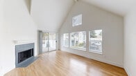 Located in Vancouver, WA, this two-story, 3-bedroom, 2-bathroom home offers a well-designed layout across two floors. The main level features an open living room with soaring vaulted ceilings, large windows that fill the space with natural light, and a tiled fireplace as a central focal point. Sliding glass doors lead to a private outdoor deck overlooking mature trees and the surrounding neighborhood. Light wood-tone flooring runs throughout the main living areas, complementing the bright, white walls and clean aesthetic.

The kitchen is thoughtfully updated with two-tone cabinetry — white upper cabinets paired with slate-blue lowers — a geometric tile backsplash, stainless steel appliances, a deep single-basin sink with a matte black pull-down faucet, and track lighting overhead. The main level also includes additional bedrooms with light wood flooring and natural light from side-facing windows.

Upstairs, the primary bedroom features carpeted flooring, a sliding closet, vaulted ceilings, and a window with neighborhood views. The bathrooms are finished with warm wood-tone flooring, gray cabinetry, white countertops, and modern black hardware accents. A dedicated laundry area with a full-size washer and dryer completes this functional and stylish home.