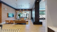 This elegantly designed single-floor amenity space delivers a refined, hospitality-inspired atmosphere through thoughtful architectural details and high-end finishes throughout. The main lounge area anchors the space with warm caramel leather sofas, layered area rugs, and a dramatic cluster of copper globe pendant lights suspended from the soaring ceiling, creating an inviting focal point. A bold dark stone structural column houses a sleek linear fireplace, adding warmth and definition to the open floor plan. Floor-to-ceiling windows along the perimeter flood the interior with natural light and offer verdant outdoor views, while sheer white drapery provides an elegant softening element. A built-in bar with tall black stools is positioned along the window line, ideal for casual socializing. The catering kitchen features dark wood cabinetry, white marble countertops, a large central island with bar seating, and a striking geometric tile floor that transitions seamlessly into the light hardwood throughout the space. A separate dining and collaborative area offers round marble-top tables with mixed-tone seating and a mounted display screen, suited for both casual gatherings and meetings. An art-gallery-inspired nook showcases a curated wall of colorful framed prints above tufted emerald green bench seating, adding a vibrant artistic element to the overall design.