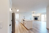 Located in Gretna, Nebraska, this well-appointed 2-bedroom, 2-bathroom residence offers a thoughtfully designed single-floor layout with modern finishes and a bright, welcoming atmosphere. The open-concept kitchen and living area serves as the heart of the home, showcasing white shaker cabinetry, quartz countertops, a large center island with a black matte faucet and sink, and stainless steel appliances including a refrigerator, range, and microwave. Light wood-look flooring flows throughout the main living areas, complementing the clean, neutral palette. The living room is anchored by a striking corner fireplace clad in stacked stone tile with a rustic wood mantel, and a sliding glass door opens to a private balcony with neighborhood views. Both bedrooms feature plush carpet, ceiling fans, and walk-in closets with built-in shelving. The bathrooms are finished with white cabinetry, quartz countertops, and matte black hardware, with one offering a tub-shower combination. A dedicated laundry room accommodates full-size washer and dryer units. A skylight in the kitchen area adds an extra touch of natural light, enhancing the overall airy and modern ambiance of this move-in-ready home.