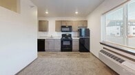 Located at 7412 E 26th St in Sioux Falls, South Dakota, this single-floor unit offers a practical and well-organized layout designed to maximize every square foot. The entrance leads into a central hallway that connects all areas of the space, with the electrical panel and thermostat conveniently accessible along the corridor wall. Wood-look flooring runs through the entryway and kitchen area, transitioning to carpet in the living space, adding warmth and texture throughout.

The combined dining room, kitchen, and living room forms the heart of the unit. The kitchen is equipped with taupe-toned cabinetry, a full suite of black appliances including a range, over-the-range microwave, refrigerator, and dishwasher, along with a light countertop and a single-basin sink. The open living area benefits from natural light through a window, recessed lighting, and a ceiling fan, creating a comfortable and airy atmosphere.

The full bathroom features a tub/shower combination, toilet, and a vanity with wood-toned cabinetry and a light countertop, all finished in a clean, white palette with wood-look flooring. A dedicated laundry area with a washer and dryer rounds out the unit's functional offerings, adding everyday convenience to this neatly designed space.