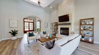 This well-appointed clubhouse in Jacksonville, Florida offers a thoughtfully designed single-floor layout that balances elegance with everyday functionality. The centerpiece of the space is a dramatic main lounge area distinguished by soaring ceilings, a floor-to-ceiling natural stone fireplace with a mounted flat-screen TV, and wide-plank hardwood-style flooring throughout. A coffered ceiling detail with a ceiling fan adds architectural interest overhead, while elegant crown molding frames the room. An arched entryway connects the main lounge to an adjacent foyer, where rich wood-framed French doors invite natural light and offer views of the lush outdoor surroundings. A secondary seating area near oversized windows provides a bright, airy retreat with palm tree views, enhanced by curated artwork and warm accent lighting. The fully equipped kitchen features gray shaker-style cabinetry, white quartz countertops, stainless steel appliances including a dishwasher, microwave, and refrigerator, and a large undermount sink — ideal for hosting and catering needs. A dedicated conference or meeting room offers a refined setting with a long dining table, upholstered chairs, dual round wood-framed mirrors, and a striking linear pendant light fixture, making it well-suited for private gatherings or meetings.