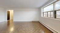 This 2-bedroom, 1-bathroom unit at 14 Westdale Dr in Welland, Ontario offers a functional and comfortable layout across a single floor. The spacious living room is a standout feature, with classic parquet flooring, bright white walls, large windows that invite natural light, and a baseboard heating system running along the exterior wall. The open sightlines from the living area extend toward a private balcony, which offers elevated treetop views of the surrounding neighbourhood.

The kitchen has been thoughtfully updated with white shaker-style cabinetry, subway tile backsplash, dark countertops, and stainless steel appliances including a full-size refrigerator and dishwasher. Light tile flooring completes the clean, modern aesthetic.

Both bedrooms feature the same warm parquet flooring found throughout the unit. The primary bedroom is generously sized and includes a double-door closet. The second bedroom also includes a closet and benefits from a window with a natural, tree-lined outlook and a classic cast-iron radiator. The full bathroom is finished with crisp white subway tile surrounding a soaker tub and shower combination. A hallway connects all rooms, providing a logical and efficient flow throughout the unit.