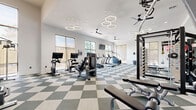 Located at 1501 Bellamy Pl in Louisville, KY, this fitness center offers a spacious, single-floor layout designed to support a full range of workout routines. The space is finished with a striking two-tone checkered tile floor in gray and white, giving it a clean, modern aesthetic throughout.

Natural light fills the room through multiple large windows positioned along the walls, offering views of the surrounding outdoor greenery and keeping the atmosphere open and inviting. Ceiling fans are distributed across the space to maintain comfortable airflow, while geometric hexagonal pendant lights add a contemporary design touch overhead.

The fitness center is comprehensively equipped to meet a variety of training needs. A dedicated cardio zone features several treadmills and elliptical machines, each equipped with individual screens. Stationary cycling bikes with digital monitors are also available for low-impact training. The strength training area includes a power rack, cable machines, and a selection of weight benches suited for a range of exercises.

A free weights section provides kettlebells, dumbbells, medicine balls, and resistance bands neatly organized on a dedicated rack. Full-length mirrors line one wall, enhancing the sense of space and supporting proper form during workouts. Mounted flat-screen TVs are positioned throughout the room, adding to the functionality of the space. Overall, this fitness center delivers a well-organized and energizing environment for residents.