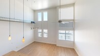 This contemporary loft-style residence in Phoenix, Arizona offers a striking two-floor layout that maximizes both space and style. The main level is anchored by a well-appointed kitchen featuring rich dark wood cabinetry, granite countertops, a subway tile backsplash, and a full suite of stainless steel appliances including a range, microwave, dishwasher, and refrigerator. A central kitchen island with an integrated sink adds both functionality and visual appeal, while track lighting illuminates the space with a modern touch. The open living area commands attention with soaring double-height ceilings and an abundance of natural light streaming through large, stacked windows that reach toward the ceiling, creating an airy, expansive atmosphere. Light hardwood flooring flows throughout both levels, enhancing the bright and clean aesthetic. A dramatic spiral staircase with sleek metal railings leads to the upper loft level, which features a modern gate at the landing — ideal as a private bedroom retreat. The full bathroom on the main floor is clean and functional, complete with a tiled tub/shower combination and contemporary fixtures. A hallway connects the key areas seamlessly. This thoughtfully designed loft blends urban sophistication with practical living in the heart of Phoenix.
