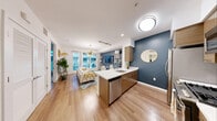 This contemporary residence at Next On Lex is designed with a seamless open-concept layout that connects the kitchen, dining, and living areas into one cohesive, light-filled space. Rich hardwood-style flooring runs throughout, complemented by crisp white ceilings and bold navy accent walls that add a modern, sophisticated character.

The kitchen is well-appointed with warm wood cabinetry, stainless steel appliances including a gas range, microwave, refrigerator, and dishwasher, along with a sleek white quartz peninsula that doubles as a breakfast bar. A tile backsplash and contemporary fixtures complete the culinary space.

The living room features floor-to-ceiling windows and direct access to a private balcony with glass railings, offering views of lush landscaping and the surrounding urban streetscape. A striking sputnik chandelier serves as a design centerpiece.

The bedroom is a calm retreat with large windows, a ceiling fan, and ample natural light. The bathroom is finished with a floating wood vanity, a quartz countertop, an undermount sink, and a backlit frameless mirror set against clean, neutral tile.

The private balcony provides a serene outdoor escape overlooking a beautifully landscaped courtyard and the vibrant neighborhood beyond, rounding out this well-crafted urban residence.