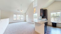 This single-floor home in Cayce, South Carolina offers a well-designed layout across three bedrooms and two bathrooms. The standout feature of the main living area is its dramatic vaulted ceiling, which creates a remarkably open and airy atmosphere. A ceiling fan anchors the space, while multiple windows along the front wall flood the room with natural light. Soft carpeting extends throughout the living area, adding warmth underfoot.

The kitchen flows seamlessly from the living room and features dark cabinetry, stainless steel appliances including a refrigerator and range, and a peninsula with a built-in sink and pendant lighting above. Hard-surface flooring runs through the kitchen, providing a practical contrast to the carpeted living spaces.

The primary bedroom is generously sized and connects directly to a private bathroom equipped with dark vanity cabinetry, a single sink, and a soaking tub. A dedicated walk-in closet with wire shelving offers substantial storage. The second bathroom mirrors the dark cabinetry aesthetic and includes a tiled tub-shower combination with wood-look flooring. The two additional bedrooms are bright and carpeted, each benefiting from natural light through large windows.