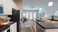 This single-floor residence showcases a cohesive modern design with warm neutral tones, light wood-style flooring, and an abundance of natural light throughout. The open-concept kitchen is a standout feature, equipped with stainless steel appliances including a French door refrigerator, electric range, and built-in microwave. White shaker cabinetry extends to the ceiling, providing generous storage, while a central island with dark granite countertops and an undermount sink doubles as a casual dining and prep space. Pendant lighting above the island adds a refined touch. The living area is bright and welcoming, anchored by a glass-paneled exterior door flanked by large windows fitted with white blinds that allow for controlled natural light. A ceiling fan adds comfort to the space. The bedrooms are well-proportioned, each featuring large windows that bring in natural light, and light wood-style flooring that continues from the main living areas. The bathroom is finished with the same dark granite countertops as the kitchen, white cabinetry, a large framed mirror, and clean tile flooring, creating a consistent and polished aesthetic. Overall, this residence offers a thoughtfully designed, move-in-ready living environment with stylish, contemporary finishes at every turn.