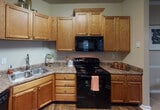This single-story residence located on Raven Grove Way in Knoxville, Tennessee, offers a well-organized layout with distinct living spaces throughout. The kitchen is equipped with warm honey-toned cabinetry extending to the ceiling, laminate countertops, a double stainless steel sink, and black appliances including a range, dishwasher, refrigerator, and built-in microwave, providing ample storage and functionality. Wood-style flooring grounds the kitchen area, adding a cohesive, practical finish.

The living room features neutral-toned walls, carpet flooring, crown molding, a ceiling fan with light fixture, and access to an exterior door framed by windows with blinds and sheer curtains, allowing natural light to fill the space. Adjacent to the living area, the dedicated dining space includes crown molding, chair rail detailing, carpet flooring, and a pendant light fixture overhead.

The bedrooms are carpeted and include ceiling fans and windows with blinds that invite natural light and outdoor views. The bathroom features wood-style flooring, a vanity with warm cabinetry, a tub-shower combination, and built-in wall shelving for additional storage, presenting a clean and practical design throughout.