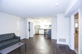 This single-floor unit offers a well-organized layout designed for comfortable everyday living. The kitchen is equipped with stainless steel appliances, including a range, built-in microwave, dishwasher, and refrigerator. White cabinetry lines the walls, complemented by dark countertops that provide a clean contrast. Rich dark hardwood-style flooring runs throughout the kitchen and living areas, adding warmth and cohesion to the space. A compact kitchen island with bar seating offers an additional dining option. The living room is open and inviting, featuring a sliding glass door dressed with vertical blinds that floods the space with natural light and provides access to an outdoor balcony with views of surrounding greenery. The bedrooms are carpeted for comfort, each offering closet storage — one with a mirrored sliding door closet and another with access to an en-suite bathroom. The bathroom features a full tub-shower combination with chrome fixtures set against clean, neutral walls. Throughout the unit, textured ceilings and neutral wall tones create a simple, functional aesthetic. A ceiling fan in the kitchen area adds to the unit's practicality, making this a well-appointed space suited for efficient, comfortable living.