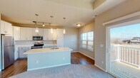 This single-floor residence offers a thoughtfully designed open-concept layout that seamlessly connects the kitchen, dining, and living areas. The kitchen is a standout feature, showcasing white shaker-style cabinetry extending to the ceiling, a large center island with a built-in sink and light countertops, stainless steel appliances including a refrigerator, microwave, and range, and pendant lighting complemented by a track lighting system. Wood-look flooring anchors the kitchen and dining zone, while plush carpeting flows throughout the living and bedroom areas.

The living room is bathed in natural light through a sliding glass door that opens to a private balcony, offering outdoor views. A tile-surround fireplace with a white mantel serves as a focal point, while a tray ceiling adds architectural depth to the space.

The bedrooms are generously proportioned, featuring tray ceilings, neutral carpet, and natural light from well-placed windows. The primary bedroom includes a ceiling fan and access to a private en-suite bathroom equipped with a walk-in glass-door shower and wood-look flooring. A second full bathroom features a shower-tub combination and a white vanity. Throughout, the warm neutral palette and clean finishes create a bright, cohesive, and welcoming ambiance.
