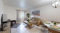 Located at 2450 S Park Rd in Pembroke Park, FL, this one-bedroom, two-bathroom residence offers a well-organized single-floor layout designed for comfortable everyday living. The open-concept living and dining area is finished with light-toned ceramic tile flooring and features a bright window with sheer curtains that invite natural light into the space. The living area provides ample room for seating and entertainment, with clean white walls that create a fresh, airy atmosphere throughout.

The kitchen is outfitted with white cabinetry, light stone-style countertops, a gray subway tile backsplash, and white appliances, including a range with over-the-range microwave. The layout is efficient and functional, flowing naturally into the dining and living areas.

The generously sized primary bedroom accommodates a full bed with ease and benefits from a window with soft draping curtains, continuing the tile flooring found throughout the unit. A dedicated closet provides additional storage.

Two bathrooms serve the residence: one features a tub-shower combination with glass sliding doors and tile surround, while the second offers a vanity with marble-style countertop and a window for natural ventilation. The overall aesthetic is light, coastal-inspired, and move-in ready.