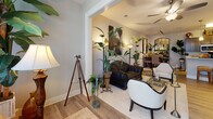 Located at 2451 Margarita Dr in Myrtle Beach, SC, this single-floor residence offers a thoughtfully designed layout with a seamless blend of coastal charm and elegant furnishings. The living area is bright and inviting, featuring light hardwood-style flooring, a ceiling fan, and an abundance of lush tropical greenery that creates a relaxed, resort-like atmosphere. Arched doorways and warm wall sconces add architectural character throughout.

The kitchen is well-appointed with dark wood cabinetry, light stone countertops, and stainless steel appliances, including a range and built-in microwave, complemented by hardwood-style flooring and ample storage.

The primary bedroom is a standout feature, showcasing a dramatic four-poster bed, plush carpeting, a ceiling fan, natural light from large windows, and direct access to a walk-in closet. A second bedroom offers a serene, cottage-inspired aesthetic with a carved white bed frame, soft carpeting, and bright windows. A third bedroom carries a cozy, intimate feel with warm accent lighting.

Two bathrooms serve the residence — one with a bathtub and shower combination with hardwood-style flooring, and another with dark wood vanity cabinetry and stone countertops. Nautical accents and coastal-themed artwork are woven throughout, reflecting the spirit of the Myrtle Beach locale.
