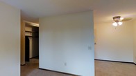 This single-floor space presents a straightforward and functional layout designed to maximize usability. The interior is finished in neutral, light tones throughout, with crisp white walls that create a bright and airy atmosphere. Carpeted flooring runs through the main areas, adding a layer of warmth and comfort underfoot, while dark baseboards provide a subtle contrast to the light walls and ceiling.

A partial wall divides the space, creating a natural separation between areas while maintaining an open feel. On one side, a closet area is visible, complete with a hanging rod and shelf, offering practical built-in storage. Electrical outlets are thoughtfully positioned along the walls, providing convenience throughout the space.

The overall ambiance is clean, simple, and move-in ready, with a neutral palette that serves as an ideal canvas for personalization. The layout is well-suited for a variety of uses, with each area flowing naturally into the next. The space is compact yet efficient, making the most of every square foot through its straightforward design and practical finishes.
