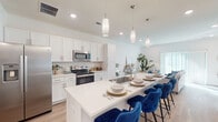This two-story home is designed with a clean, contemporary aesthetic, showcasing white walls, light wood-style flooring on the main level, and an abundance of natural light throughout. The open-concept main floor centers around a well-appointed kitchen featuring white shaker cabinetry, a white quartz countertop island with seating for multiple bar stools, stainless steel appliances including a refrigerator, range, and microwave, and a subway tile backsplash. Cylindrical pendant lights hang above the island, adding a modern touch. The kitchen flows seamlessly into the living area, which benefits from a large sliding glass door that fills the space with natural light. A carpeted staircase with a sleek metal railing leads to the upper level, where the bedrooms are located. Each bedroom features plush carpet flooring and windows that invite natural light and outdoor views of the surrounding neighborhood. The bathrooms are finished with wood-look flooring, white vanity cabinetry, and framed mirrors. A dedicated in-unit laundry area houses a full-size washer and dryer with overhead shelving for added storage. A walk-in closet adjacent to one of the bathrooms provides generous wardrobe space, completing this well-organized and functional home.