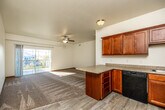 This single-floor residence is thoughtfully designed with an open layout that connects the kitchen and living areas, creating a cohesive and functional living space. The kitchen is well-appointed with rich medium-toned wood cabinetry, granite-style countertops, and a full suite of black appliances including a range, dishwasher, and refrigerator. Light wood-look flooring runs throughout the kitchen, complementing the warm cabinetry tones and providing a clean, durable surface.

The living area is generously sized, featuring neutral-toned carpet, a ceiling fan with light fixture, and a sliding glass door that opens to a private balcony overlooking a residential neighborhood — allowing abundant natural light to fill the space. The bedrooms are carpeted and well-proportioned, each benefiting from large windows that frame outdoor views of greenery and open skies. Warm wood-toned interior doors and coordinating baseboards provide consistent, cohesive detailing throughout the unit. Closet space is present in the bedroom areas, adding practical storage. Overall, the space presents a clean, neutral palette with warm wood accents, offering a comfortable and functional living environment.