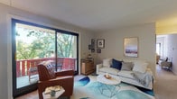 This thoughtfully designed single-floor residence offers a comfortable and cohesive layout across its key living spaces. The living room serves as the heart of the home, featuring large sliding glass doors that open onto a private balcony overlooking lush, mature trees. Natural light pours into the space, highlighting the stylish furnishings, including a tufted leather accent chair, a plush white sofa, and a bold blue abstract area rug. Curated wall art and warm accent lighting contribute to an inviting, relaxed atmosphere. The balcony itself provides a peaceful outdoor retreat with seating surrounded by verdant greenery. The kitchen is equipped with warm oak cabinetry, dark granite countertops, hardwood flooring, and a full suite of white appliances, including a refrigerator, range, microwave, and dishwasher. A peninsula counter adds additional prep space and visual separation. The bedroom is a serene and restful retreat, featuring soft neutral tones, a ceiling fan, a spacious closet, and a cozy seating area. Rustic wood nightstands and a coordinated dresser lend a warm, grounded character to the room. The bathroom is clean and functional, finished in bright white with tile flooring, a vanity with cabinet storage, and a shower-tub combination.