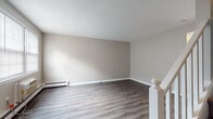 This three-floor residence in Manchester, Connecticut offers a thoughtfully laid-out living environment with a clean, neutral aesthetic throughout. The main living areas feature durable hardwood-style flooring in a warm gray tone, complemented by crisp white trim and baseboard heating. A staircase with white railings connects the floors, providing a cohesive flow through the home.

The kitchen is a standout feature, showcasing white cabinetry with arched detailing, granite-style countertops, a white subway tile backsplash, and a full suite of stainless steel appliances including a refrigerator, range, and dishwasher. Natural light filters into the living spaces through windows fitted with blinds, enhancing the bright and airy feel of the interior.

The upper levels are carpeted throughout, lending a comfortable, quieter atmosphere to the sleeping quarters. Bedrooms are generously sized with neutral wall tones, offering flexibility for various furnishing arrangements. A walk-in closet provides abundant storage with built-in shelving on multiple walls. Additional hallway space on the upper floors connects the rooms efficiently. The multi-level layout of this Manchester home provides distinct zones for living, dining, and rest, making it a functional and inviting space.