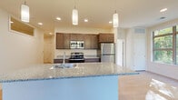 Located at 350 Bishops Way in Brookfield, Wisconsin, this well-appointed single-floor residence offers three bedrooms, two bathrooms, and a thoughtfully designed layout. The open-concept kitchen, dining, and living area serves as the heart of the home, featuring rich dark-stained cabinetry, granite countertops, stainless steel appliances, and a large island with a built-in sink. Stylish pendant lighting and recessed fixtures illuminate the space, while light-toned hardwood-style flooring adds warmth throughout the main living areas. A large window in the kitchen and living zone frames lush outdoor greenery, filling the space with natural light. The bedrooms are finished with plush carpeting and include generous closet space; the primary bedroom is a comfortable size and benefits from a ceiling fan and a sizable window overlooking the natural surroundings. Both bathrooms are finished with granite-topped dark wood vanities, large mirrors, and hardwood-style flooring, with one bathroom featuring a full tub-shower combination. A dedicated laundry area houses a stacked washer and dryer unit, adding everyday convenience. A utility room and hallway with additional closets round out the practical layout of this move-in-ready Brookfield residence.