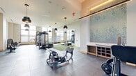 Located at 340 E Paces Ferry Rd NE in Atlanta's prestigious Buckhead neighborhood, this expansive fitness center offers a premier exercise experience across a generously sized single-floor layout. The facility is defined by its striking architectural design, highlighted by dramatic floor-to-ceiling glass curtain walls that flood the space with natural light and frame sweeping panoramic views of the Atlanta skyline.

The exercise floor is thoughtfully organized into distinct functional zones. A dedicated cardio area houses a row of treadmills and elliptical machines positioned directly in front of the expansive glass walls, allowing users to enjoy the city views during their workouts. A separate strength training zone features a multi-station cable machine, free weights, a leg press, rowing machines, and an array of dumbbells on tiered racks, all set on durable rubber flooring. A dedicated studio area with light wood flooring, a tray ceiling with recessed lighting, and glass partition walls provides an ideal space for cycling classes or stretching.

Throughout the facility, large-format tile flooring, full-length mirrors, and stylish pendant lighting contribute to a polished, contemporary ambiance. Decorative artwork and built-in cabinetry add refined touches, while large ceiling fans and glass-paneled doors ensure comfort and easy access. The space delivers a cohesive, high-end fitness environment suited for a comprehensive workout regimen.