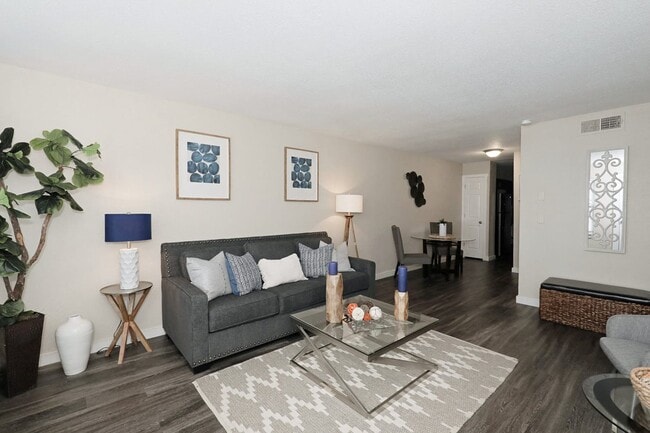 Spacious living room with dark hardwood floors, gray sofa, glass coffee table, framed blue artwork, and indoor tree - Bennett Pointe