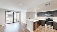 This single-story space showcases a clean, contemporary design with wood-look flooring running consistently throughout every room, creating a cohesive and polished aesthetic. The open-concept kitchen serves as a central highlight, featuring dark espresso cabinetry that contrasts sharply against bright white quartz countertops. A peninsula with an undermount sink provides additional workspace and casual seating potential. Stainless steel appliances, including a refrigerator, range, microwave, and dishwasher, complete the well-equipped kitchen. Recessed lighting illuminates the space efficiently overhead.

The living area benefits from abundant natural light, delivered through a striking black-framed multi-pane sliding glass door that opens to an outdoor area. This architectural detail adds a modern industrial character to the otherwise clean, white-walled interior. The bedrooms are bright and well-proportioned, with one featuring mirrored sliding closet doors and black-framed windows that further reinforce the contemporary style.

The bathrooms are finished in a crisp, all-white palette, each equipped with a tub-shower combination enclosed by sliding glass doors, a white vanity, and wood-look flooring that ties seamlessly into the rest of the unit. Overall, the space presents a fresh, move-in-ready environment with consistent modern finishes throughout.
