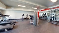 Located in Andover, Kansas, this fitness center offers a comprehensive workout facility designed to accommodate a wide range of exercise routines. The space is laid out on a single floor and makes efficient use of its footprint to provide a full suite of fitness amenities.

The interior features a durable rubber flooring surface throughout, well-suited for both heavy equipment and high-impact workouts. Recessed and flush-mounted ceiling lighting ensures the space is evenly and brightly illuminated. A bold red accent wall paired with large wall-mounted mirrors enhances the sense of openness and adds a dynamic, energizing aesthetic to the environment.

The cardio zone is positioned along the windowed wall, where treadmills, elliptical machines, and stationary bikes are arranged to take advantage of natural light and outdoor views, creating an inviting atmosphere for endurance training. The strength training area is well-stocked with a cable crossover machine, a multi-function weight rack, free weights, and benches, offering versatile options for resistance-based workouts. Spin bikes are also available for cycling-focused sessions.

A dedicated functional fitness corner houses stability balls, resistance bands, and exercise mats, providing space for stretching, balance training, and accessory work. The clean, organized layout and variety of equipment make this fitness center a comprehensive and practical facility for users of all fitness levels.