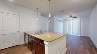 This single-floor unit offers a thoughtfully designed open-concept layout that seamlessly integrates the kitchen and living area into one cohesive space. The kitchen is a standout feature, equipped with a granite-topped peninsula island with a built-in double sink, rich dark-wood cabinetry, stainless steel appliances including a refrigerator, range, and microwave, and a tile backsplash. Pendant lighting hangs above the island, while track lighting illuminates the kitchen zone. Wood-style flooring runs throughout the entire unit, adding warmth and continuity to every room. The living area benefits from a ceiling fan, vertical blinds allowing natural light to filter in, and an open flow that makes the space feel airy and functional. The bathroom features matching dark-wood cabinetry with a single-sink vanity, a large mirror, wall-mounted lighting, a tub-shower combination with tiled surround, and the same wood-style flooring for a consistent aesthetic. A dedicated closet provides convenient built-in storage. Clean white walls and a neutral palette throughout create a bright, modern ambiance well-suited for a variety of interior styles.