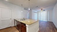 This single-floor unit offers a thoughtfully designed open-concept layout that seamlessly integrates the kitchen and living area into one cohesive space. The kitchen is a standout feature, equipped with a granite-topped peninsula island with a built-in double sink, rich dark-wood cabinetry, stainless steel appliances including a refrigerator, range, and microwave, and a tile backsplash. Pendant lighting hangs above the island, while track lighting illuminates the kitchen zone. Wood-style flooring runs throughout the entire unit, adding warmth and continuity to every room. The living area benefits from a ceiling fan, vertical blinds allowing natural light to filter in, and an open flow that makes the space feel airy and functional. The bathroom features matching dark-wood cabinetry with a single-sink vanity, a large mirror, wall-mounted lighting, a tub-shower combination with tiled surround, and the same wood-style flooring for a consistent aesthetic. A dedicated closet provides convenient built-in storage. Clean white walls and a neutral palette throughout create a bright, modern ambiance well-suited for a variety of interior styles.