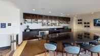 Located at 901 H St NE in Washington, DC's vibrant NoMa/H Street corridor, this thoughtfully designed amenity floor offers a diverse range of social and recreational spaces unified by a bold, eclectic aesthetic. The entry lobby commands attention with its intricate geometric parquet flooring, a sweeping gold-accented ceiling detail, and clusters of emerald green velvet seating beneath dramatic pendant lights—setting a sophisticated tone throughout.

The lounge area features a plush sectional sofa, a large built-in media wall flanked by dark wood cabinetry, and expansive windows that flood the space with natural light and neighborhood views. A dedicated dining area is anchored by an oval table with artistic pendant fixtures above, and floor-to-ceiling sliding glass doors that open directly onto an outdoor terrace complete with lounge furniture.

A standout fireplace nook showcases a stone surround with curated book storage, framed by large windows on either side offering terrace views—creating an inviting retreat. The full-service bar area presents a sleek black granite countertop, dark cabinetry, industrial-style open shelving, and bar seating, ideal for social gatherings. A game room with arcade machines and additional seating rounds out the offerings, ensuring a well-appointed space for both relaxation and entertainment.