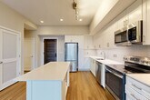 Located at 3400 South Clark Street in Arlington, VA, this well-appointed 2-bedroom, 2-bathroom residence offers a thoughtfully designed single-level layout. The open-concept kitchen and dining area serves as the heart of the home, showcasing crisp white shaker-style cabinetry extending to the ceiling, white quartz countertops, a subway tile backsplash, and a full suite of stainless steel appliances including a refrigerator, range, dishwasher, and built-in microwave. A freestanding white kitchen island provides additional prep space and storage. Warm-toned hardwood-style flooring flows throughout the main living areas, complementing the neutral palette. The spacious living room is a standout feature, anchored by dramatic floor-to-ceiling windows that frame sweeping urban views of the Arlington skyline, flooding the space with natural light. The generously sized primary bedroom includes a double-door closet and connects to the hallway. Both bathrooms are finished with large-format tile flooring and white vanities; one features a tiled tub-shower combination. Additional highlights include an in-unit laundry area, multiple closets for ample storage, and a welcoming entryway with a distinctive blue front door.