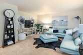 This single-floor residence is thoughtfully laid out to maximize comfort and functionality across its living spaces. The living room serves as the centerpiece of the home, featuring plush wall-to-wall carpeting, neutral-toned walls, and large windows dressed with sheer curtains that allow natural light to filter through. A generously sized sectional sofa anchors the space, complemented by a cowhide area rug and tasteful wall art, creating a relaxed yet stylish atmosphere.

The kitchen is well-equipped with warm wood cabinetry in both light and medium tones, a peninsula with a laminate countertop that doubles as a casual dining or prep area, and a full suite of white appliances including a refrigerator, range, and dishwasher. Tile flooring and recessed lighting add to the kitchen's practical design.

The bedrooms are carpeted and feature windows with blinds and colorful curtain panels, providing privacy and natural light. A textured ceiling adds visual character to the sleeping spaces.

The bathroom includes a wide vanity with ample storage, a large mirror with overhead lighting, tile flooring, and a tub-shower combination, offering a clean and functional layout. Throughout, the home maintains a warm, cohesive palette with neutral walls and consistent finishes.
