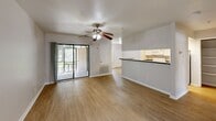 Located on Blanco Road in San Antonio, Texas, this one-bedroom, one-bathroom unit offers a practical and comfortable single-floor layout. The open-concept living and kitchen area forms the heart of the home, featuring warm hardwood-style flooring and a ceiling fan with light fixture overhead. Large sliding glass doors flood the living space with natural light and provide direct access to an outdoor balcony, offering pleasant views of the surrounding greenery. The kitchen is efficiently designed with white cabinetry, dark countertops, a full suite of white appliances including a range, microwave, and refrigerator, and a breakfast bar that connects seamlessly to the living area. The bedroom is carpeted for comfort, featuring a ceiling fan, a window that brings in natural light, and direct access to a dedicated walk-in closet with dual hanging rods on either side, providing ample storage. The bathroom is neatly appointed with white cabinetry, a dark speckled countertop, a tub/shower combination, and wood-style flooring that ties into the rest of the unit. Clean neutral wall tones throughout the space lend a bright, cohesive aesthetic that is both functional and inviting.