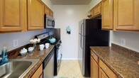 Located at 8584 Freyman Drive in Chevy Chase, Maryland, this single-floor apartment offers a practical and comfortable layout set within a well-maintained brick residential community. The exterior grounds are a standout feature, with expansive, manicured green lawns shaded by mature trees, a dedicated playground area, and a clean walkway leading to the entrance — ideal for outdoor enjoyment.

Inside, the living area is bright and open, featuring neutral-toned carpet, clean white walls, and a large sliding glass door dressed with vertical blinds that invites natural light and provides access to the outdoors. The space flows naturally into a hallway connecting the various rooms. A second carpeted living or dining area is illuminated by a classic chandelier and offers an open sightline to the kitchen.

The galley-style kitchen is efficiently designed with warm wood cabinetry, dark granite-style countertops, stainless steel appliances including a refrigerator and microwave, a gas range, and tile flooring — offering everything needed for comfortable daily living. The bathroom is clean and functional, featuring tile flooring, a vanity with wood cabinetry, and a tub-shower combination. Throughout the apartment, the neutral color palette and practical finishes create a cohesive, move-in-ready atmosphere.