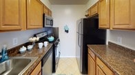 Located at 8584 Freyman Drive in Chevy Chase, Maryland, this single-floor apartment offers a practical and comfortable layout set within a well-maintained brick residential community. The exterior grounds are a standout feature, with expansive, manicured green lawns shaded by mature trees, a dedicated playground area, and a clean walkway leading to the entrance — ideal for outdoor enjoyment.

Inside, the living area is bright and open, featuring neutral-toned carpet, clean white walls, and a large sliding glass door dressed with vertical blinds that invites natural light and provides access to the outdoors. The space flows naturally into a hallway connecting the various rooms. A second carpeted living or dining area is illuminated by a classic chandelier and offers an open sightline to the kitchen.

The galley-style kitchen is efficiently designed with warm wood cabinetry, dark granite-style countertops, stainless steel appliances including a refrigerator and microwave, a gas range, and tile flooring — offering everything needed for comfortable daily living. The bathroom is clean and functional, featuring tile flooring, a vanity with wood cabinetry, and a tub-shower combination. Throughout the apartment, the neutral color palette and practical finishes create a cohesive, move-in-ready atmosphere.