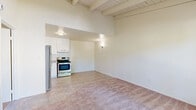 Located at 7781 Archibald Ave in Rancho Cucamonga, CA, this one-bedroom, one-bathroom unit offers a thoughtfully laid-out single-floor plan. A standout architectural feature is the vaulted ceiling with exposed white-painted wood beams, lending the living area a sense of height and openness that extends throughout the space. The living room is carpeted in neutral tones and receives natural light through a window framing views of mature surrounding trees, creating a calm, pleasant ambiance. Adjacent to the living area, the kitchen is efficiently designed with white cabinetry, light granite-style countertops, tile flooring, and stainless steel appliances including an electric range and refrigerator, complemented by an under-cabinet range hood. The bedroom is generously proportioned, featuring the same warm carpeting and vaulted beamed ceiling detail, with a window that brings in natural light and greenery views. A dedicated closet provides practical storage. The bathroom includes a full tub-shower combination with clean white surround and chrome fixtures. A wall-mounted heating unit is also present in the unit. The overall aesthetic is clean, neutral, and functional, well-suited for comfortable everyday living.