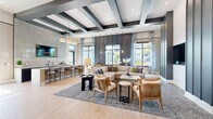 Located at 3843 Dequattro Dr in Rockledge, Florida, this single-floor space offers a thoughtfully designed interior that balances modern sophistication with welcoming comfort. The expansive living room serves as the centerpiece of the layout, showcasing striking architectural details including a dramatic coffered ceiling with bold dark beams set against crisp white panels, which draws the eye upward and amplifies the sense of volume and height throughout the space.

Light-toned wood flooring runs throughout, lending warmth and continuity to the open-concept floor plan. The living area is anchored by a generous seating arrangement featuring a large sectional sofa, rattan accent chairs, and layered area rugs that define the lounge zone. A wall-mounted flat-screen television is recessed into a sleek dark accent wall framed by tall columns, creating a refined focal point.

Natural light pours in through large windows dressed with flowing blue-and-white patterned curtains, offering views of the surrounding neighborhood. A wet bar with bar-height seating and an overhead-mounted television provides a social hub along one wall, while a set of full-height black-framed glass doors opens to an adjoining space, adding architectural interest and transparency. Curated artwork and contemporary furnishings throughout complete the polished, inviting atmosphere.