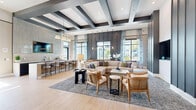 Located at 3843 Dequattro Dr in Rockledge, Florida, this single-floor space offers a thoughtfully designed interior that balances modern sophistication with welcoming comfort. The expansive living room serves as the centerpiece of the layout, showcasing striking architectural details including a dramatic coffered ceiling with bold dark beams set against crisp white panels, which draws the eye upward and amplifies the sense of volume and height throughout the space.

Light-toned wood flooring runs throughout, lending warmth and continuity to the open-concept floor plan. The living area is anchored by a generous seating arrangement featuring a large sectional sofa, rattan accent chairs, and layered area rugs that define the lounge zone. A wall-mounted flat-screen television is recessed into a sleek dark accent wall framed by tall columns, creating a refined focal point.

Natural light pours in through large windows dressed with flowing blue-and-white patterned curtains, offering views of the surrounding neighborhood. A wet bar with bar-height seating and an overhead-mounted television provides a social hub along one wall, while a set of full-height black-framed glass doors opens to an adjoining space, adding architectural interest and transparency. Curated artwork and contemporary furnishings throughout complete the polished, inviting atmosphere.