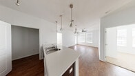 This 2-bedroom, 2-bathroom single-story residence offers a thoughtfully designed open-concept layout. The kitchen serves as the heart of the home, featuring a large peninsula island with a double stainless steel sink, white countertops, and dark espresso cabinetry that extends to the ceiling for ample storage. Pendant lighting and track lighting illuminate the space, while a full suite of appliances — including a refrigerator, range, and dishwasher — adds convenience. The kitchen flows seamlessly into the living area, which is finished with rich hardwood-style flooring, a ceiling fan, and windows with blinds that allow natural light to fill the room. The bedrooms are carpeted for comfort, with one featuring a window with outdoor views. Each bedroom is served by a dedicated closet with wire shelving for organized storage. The two bathrooms are finished consistently with dark wood vanities, white countertops, hardwood-style flooring, and clean white tiling. One bathroom includes a full soaking tub and shower combination, while the other offers a streamlined layout with a wall-mounted cabinet. A utility room rounds out the functional offerings of this well-organized residence.