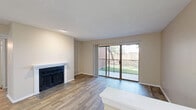 This well-appointed 2-bedroom, 2-bathroom single-floor residence offers a functional and comfortable layout. The open-concept living room is a standout space, featuring wood-style flooring, a classic fireplace with a white mantle, and a large sliding glass door that opens to a private balcony overlooking a green outdoor area, filling the room with natural light. The galley-style kitchen is efficiently designed with white cabinetry, light stone-style countertops, a breakfast bar peninsula, and black appliances including a range, microwave, and refrigerator, along with a stainless steel sink and dishwasher. The primary bedroom offers plush carpeting, a ceiling fan, a sliding door closet, and direct access to its own en-suite bathroom. The second bedroom is similarly carpeted with a ceiling fan and a walk-in closet. Both bathrooms are finished with white cabinetry, single-basin vanities, light stone-style countertops, large mirrors with overhead lighting, and a tub-shower combination. A hallway connects the bedrooms and living areas, with three closets distributed throughout the unit providing generous storage. Textured ceilings and neutral warm-toned walls are consistent throughout, creating a cohesive and inviting ambiance.