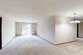 This single-story residence offers a practical and well-organized layout across three bedrooms and two bathrooms. The open combined kitchen and living area serves as the central hub of the home. The living room is generously proportioned, featuring neutral-toned carpet, white walls, and a sliding glass door that introduces natural light and outdoor views. Baseboard heating runs along the perimeter, and a pendant light fixture adds a defined touch near the dining area.

The kitchen is laid out in a galley configuration, featuring warm wood cabinetry, white countertops, hardwood-style flooring, and white appliances including a range, microwave, refrigerator, and dishwasher. A separate pantry provides additional storage directly off the kitchen.

The primary bedroom is a comfortable size, with carpeted flooring, a window for natural light, and access to a well-appointed bathroom featuring a single-sink vanity with light fixtures, a tiled shower-tub combination, and neutral finishes. A spacious walk-in closet with wire shelving provides ample storage. The two additional bedrooms are carpeted and bright, each served by baseboard heating. A hallway connects all rooms cohesively throughout the home.