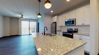 This single-floor residence in Fitchburg, Wisconsin, presents a well-appointed interior defined by contemporary finishes and a cohesive modern aesthetic throughout. The open-concept kitchen serves as the centerpiece of the living area, showcasing an expansive granite countertop island with an undermount sink and matte black faucet, complemented by pendant lighting with brass fixtures overhead. White shaker-style cabinetry lines the walls, paired with a classic white subway tile backsplash and a full suite of stainless steel appliances, including a refrigerator, electric range, and over-the-range microwave. Recessed lighting and ceiling fans are installed throughout the unit.

The living area features durable hardwood-style plank flooring and a sliding glass door with vertical blinds that allows natural light to fill the space. Bedrooms are carpeted and equipped with ceiling fans; some include windows that bring in additional daylight. Dark-trimmed doorways provide a striking contrast against the neutral white walls. The bathroom features tile flooring, a white vanity with granite countertop, a framed mirror, and a combination tub and shower. A dedicated laundry area is also present within the unit.
