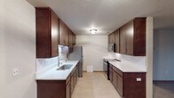 This single-floor residence offers a well-organized layout with distinct living, kitchen, bedroom, and bathroom areas. The galley-style kitchen is a standout feature, equipped with rich dark-brown cabinetry extending to the ceiling, white countertops, a subway tile backsplash, stainless steel appliances including a refrigerator, microwave, and dishwasher, and a undermount sink with a flexible faucet. Light vinyl flooring completes the functional and clean aesthetic of the space.

The living area is generously sized, featuring hard-surface flooring, warm wood trim, and a corner brick fireplace with a wood mantel that serves as a focal point. A sliding glass door provides access to an outdoor area and allows natural light to fill the room. An adjacent dining or transitional space connects seamlessly to the kitchen.

The bedrooms are carpeted and offer ample room, with one featuring a walk-in closet. Both bathrooms are finished with dark wood vanities, white countertops, large mirrors, and light vinyl flooring, maintaining a consistent design throughout. A textured ceiling is present in the kitchen, while the remaining rooms feature smooth finishes.
