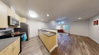 Located on Bainbridge Island, Washington, this single-floor, 2-bedroom, 1-bathroom residence offers a thoughtfully designed open-concept layout. The living area is a standout feature, boasting soaring ceilings with clerestory windows that flood the space with natural light, complemented by durable wood-look flooring throughout. The open-concept kitchen is well-equipped with light maple cabinetry, grey countertops, a full suite of stainless steel appliances including a refrigerator, microwave, range, and dishwasher, and a central peninsula with bar seating that seamlessly connects to the dining and living areas. The generously sized primary bedroom features soft carpeting, a closet, and ample room to furnish comfortably. The second bedroom is equally well-proportioned with carpeted flooring, natural light from a large window, and its own closet. The full bathroom is clean and functional, featuring wood-look flooring and a shower-tub combination. A dedicated laundry area adds everyday convenience. The interior palette of crisp white walls and neutral tones throughout creates a bright, cohesive ambiance suited for modern living in a serene Pacific Northwest setting.