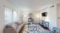 This single-floor unit offers a well-organized layout comprising a living room, kitchen, bedroom, bathroom, and two hallways. The living room serves as the central gathering space, featuring warm wood-look flooring, large windows with horizontal blinds that invite generous natural light, and a textured ceiling. The entry area transitions seamlessly into the living space via tile flooring at the front door.

The galley-style kitchen is outfitted with white shaker cabinetry, light quartz-style countertops, diagonal tile flooring, and a full suite of stainless steel appliances including a refrigerator, electric range, and dishwasher, maximizing functionality within a compact footprint.

The bedroom is a comfortable, well-proportioned room featuring wood-look flooring, a ceiling fan with light fixture, a window with natural light and outdoor views, and a bifold-door closet offering practical storage. The white walls and neutral palette contribute to a bright, airy feel.

The bathroom is finished in a clean, all-white scheme with a combination tub and shower, tile flooring, and chrome fixtures. Throughout the unit, the consistent use of light tones and natural light creates a cohesive, refreshing ambiance.