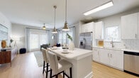 This single-story residence at 3795 Bismarck Ct in Oxford, Florida offers a thoughtfully designed open-concept layout with contemporary finishes throughout. Light wood-tone flooring extends across the main living areas, creating a cohesive and airy atmosphere.

The kitchen is well-appointed with white shaker-style cabinetry, white subway tile backsplash, stainless steel appliances including a French door refrigerator, electric range, microwave, and dishwasher. A central island with white countertops and seating provides both workspace and casual dining. Brushed nickel pendant lights hang above the island, adding a refined touch.

The open living area flows seamlessly from the kitchen, bathed in natural light from multiple large windows dressed with plantation shutters and sheer drapery. The space accommodates comfortable seating arrangements with views to the outdoors.

The bedrooms feature plush carpeting, ceiling fans, and windows that invite natural light. Each room offers a calm, neutral palette ideal for rest and relaxation. The bathroom includes a whitewashed vanity with white countertop, brushed nickel fixtures, a framed mirror with bar lighting, and wood-tone flooring consistent with the rest of the home. Overall, the residence presents a clean, modern aesthetic with practical, well-considered design.