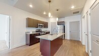 This single-floor residence is designed with a clean, contemporary aesthetic that carries consistently through each room. The kitchen serves as the centerpiece of the living space, showcasing dark espresso cabinetry paired with speckled granite countertops along the perimeter and a generously sized central island. The island features an undermount sink and is illuminated by pendant lighting suspended from above, creating a practical and visually appealing focal point. Stainless steel appliances, including a gas range, built-in microwave, and French door refrigerator, complete the kitchen's modern finish. Light wood-style flooring runs throughout the main living and kitchen areas, contributing to a bright and cohesive feel.

The bathrooms mirror the kitchen's design language, featuring matching dark cabinetry with granite-topped vanities, undermount sinks, and large wall-mounted mirrors with overhead lighting. The clean white walls and light flooring keep the spaces feeling open and airy.

The bedrooms offer a contrast in texture, with plush neutral-toned carpeting underfoot and sliding windows that allow natural light to fill each room. The overall layout, as seen in the dollhouse view, is thoughtfully organized with well-defined spaces that flow naturally from one to the next.